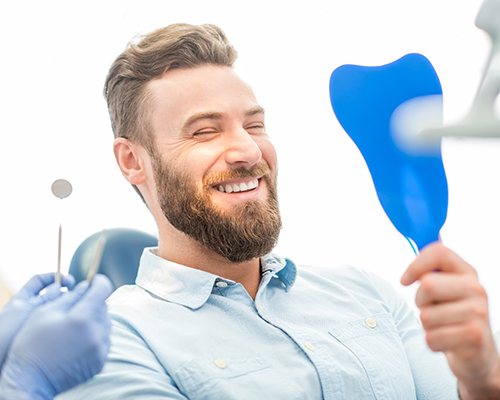 Man looking in mirror smiles at his dental bridges in Center