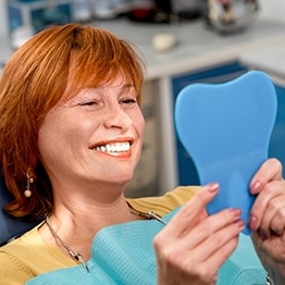Older redheaded woman in dental chair looking at her smile in a mirror