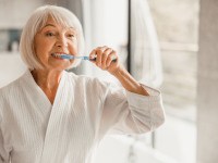 Woman smiling while brushing her teeth in bathroom