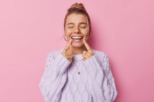 Woman on pink background pointing to her smile