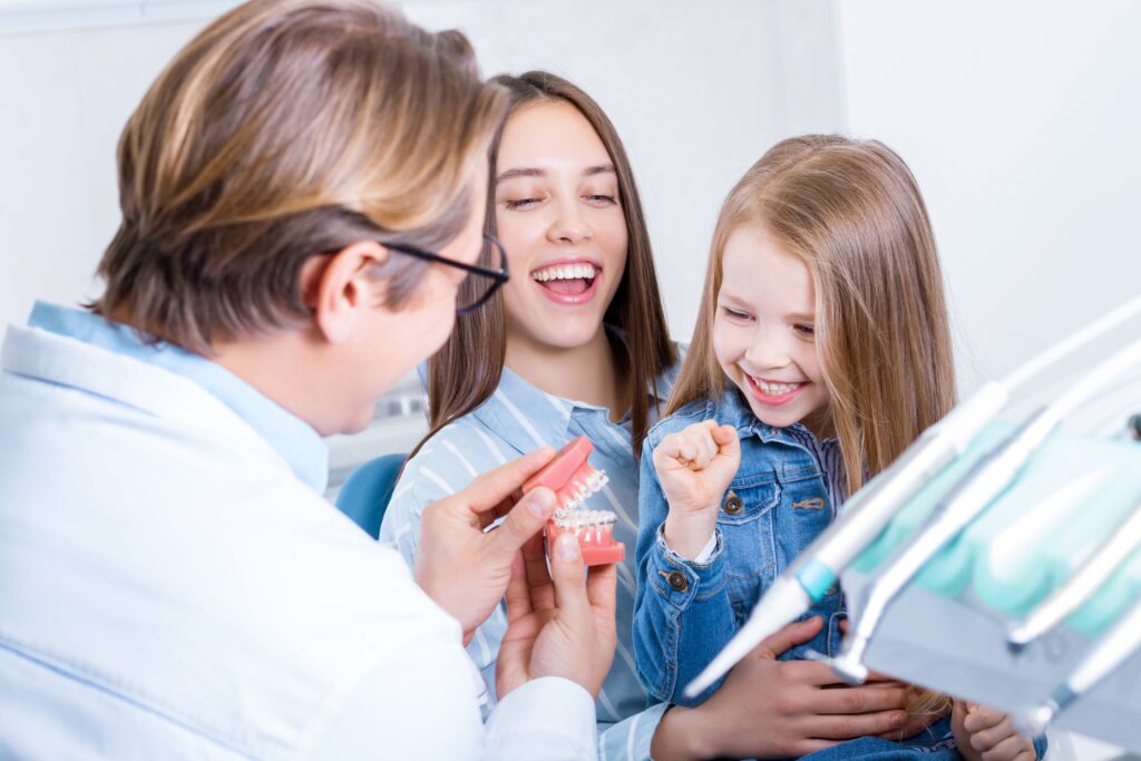 Dentist showing smiling mother and daughter model of teeth