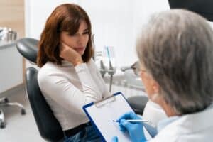 Dentist with a clipboard talking with a patient in the dental chair – read “Why Choose Our Emergency Dentist in Center”
